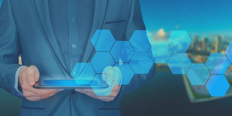 Business professional holding a tablet with digital hexagon overlay, symbolizing cybersecurity oversight and strategic information security governance.