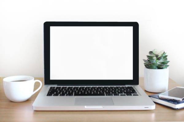 Tidy workstation showing a clean desk setup with a laptop, smartphone, coffee mug, and a small plant—an example of good clean desk policy practice.
